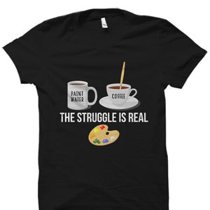 May include: Black t-shirt with a white coffee cup and a white mug with the text "Paint Water" and "Coffee". Below the cups is a paint palette and the text "The Struggle Is Real".