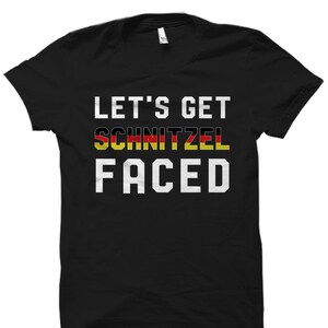 Puede incluir: Camiseta negra con texto blanco que dice "Let's Get Schnitzel Faced". La palabra "Schnitzel" est&aacute; en los colores de la bandera alemana.