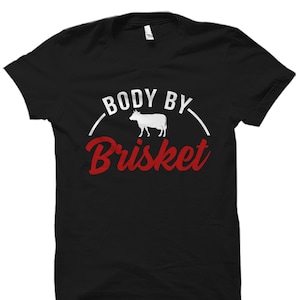 Puede incluir: Camiseta negra con texto blanco que dice "Body By Brisket" y una silueta blanca de una vaca.