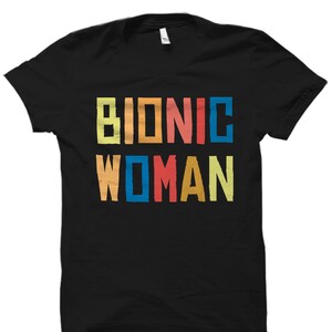 K&ouml;nnte beinhalten: Schwarzes T-Shirt mit dem Text "Bionic Woman" in bunten Blockbuchstaben.