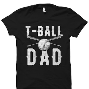 May include: Black t-shirt with a white graphic design that says "T-Ball Dad" with a baseball and crossed bats.