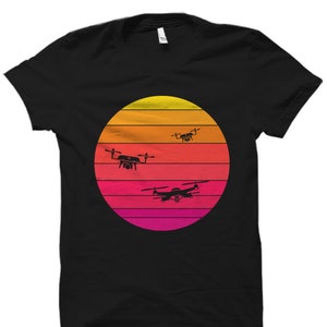 May include: Black t-shirt with a retro sunset graphic featuring three silhouettes of drones flying in the sky.