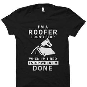 May include: Black t-shirt with white text that reads "I'm a roofer I don't stop when I'm tired I stop when I'm done". The shirt also features a white illustration of a roof and a nail gun.