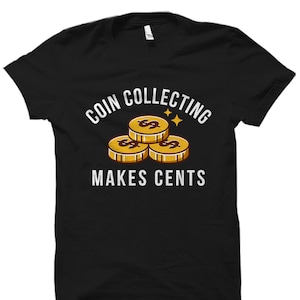 May include: Black t-shirt with a white graphic of three gold coins stacked on top of each other. The text "Coin Collecting Makes Cents" is printed in white below the coins.