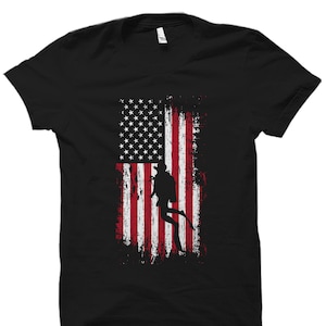 Puede incluir: Camiseta negra con un dise&ntilde;o de bandera estadounidense desgastada y una silueta de un buceador en el centro.