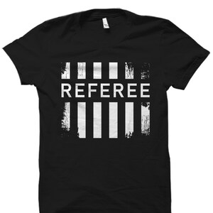 May include: Black t-shirt with a white graphic design of the word "REFEREE" in all caps with five vertical white stripes above and below the word.