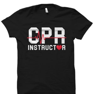 May include: Black t-shirt with white text that reads "CPR Instructor" with a red heart and a red heartbeat graphic.