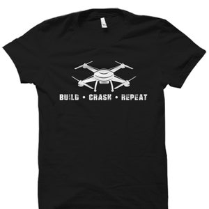 Puede incluir: Camiseta negra con un gr&aacute;fico de dron blanco y el texto "BUILD  CRASH  REPEAT".