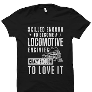 May include: Black t-shirt with white text that reads "Skilled enough to become a locomotive engineer. Crazy enough to love it."  A black and white illustration of a train is in the center of the text.