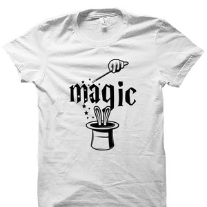 May include: White t-shirt with a black graphic of a magician's hat with a rabbit popping out, a wand, and the word "magic" in a stylized font.