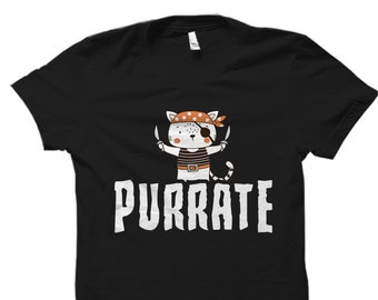 May include: Black t-shirt featuring a cartoon pirate cat design. The cat wears an eye patch and bandana, holding two crossed swords. The word "PURRATE" is printed in white below the cat illustration. A fun, whimsical design.