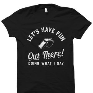 May include: Black t-shirt with white text that reads "Let's Have Fun Out There! Doing What I Say" and a white whistle graphic.