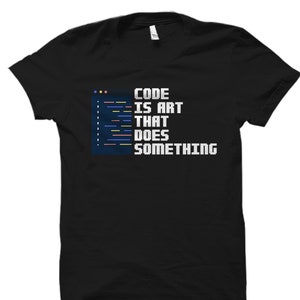 Puede incluir: Camiseta negra con texto blanco que dice "CODE IS ART THAT DOES SOMETHING" con un gráfico de código azul, amarillo y rojo.