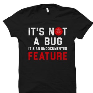 May include: Black t-shirt with white text that reads "It's not a bug. It's an undocumented feature." The text is in a bold font. There is a red circle with a white bug inside the circle above the text.