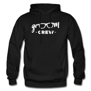 May include: Black hooded sweatshirt with a front pocket and white text that reads "groom" with glasses and "-CREW-". The sweatshirt has a drawstring hood and long sleeves.