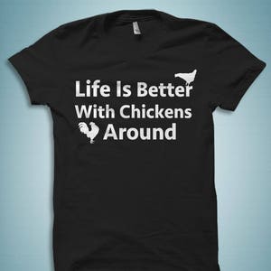 Pu&ograve; includere: Maglietta nera con testo bianco che recita "Life is Better With Chickens Around". Il testo &egrave; accompagnato da due silhouette di polli bianche.