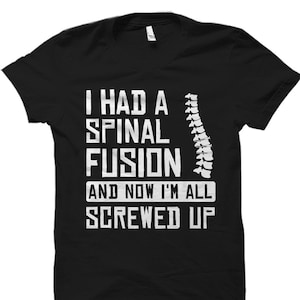 May include: Black t-shirt with white text that reads "I had a spinal fusion and now I'm all screwed up". A white outline of a spine is to the right of the text.