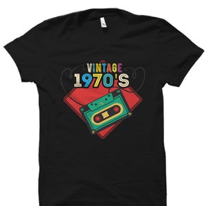 Może przedstawiać: Czarny T-shirt z vintage'owym wzorem z lat 70. z kasetą w kolorze czerwonym, ż&oacute;łtym, niebieskim, zielonym i r&oacute;żowym.