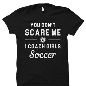 May include: Black t-shirt with white text that reads "You don't scare me I coach girls soccer" and a soccer ball graphic.