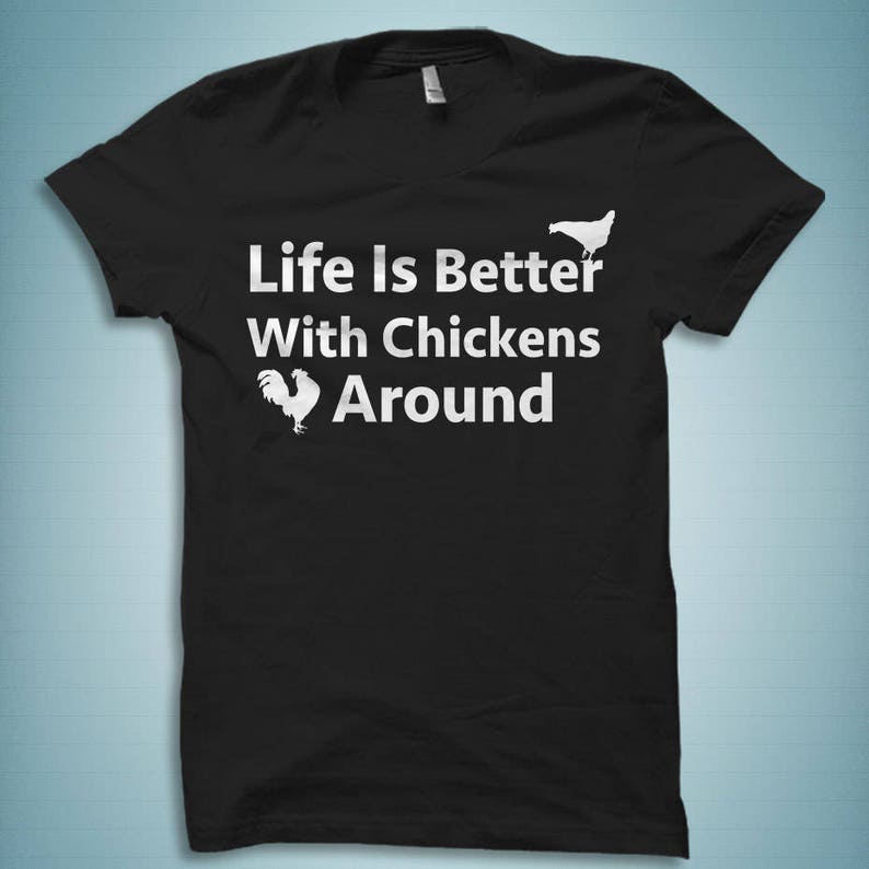 Pu&ograve; includere: Maglietta nera con testo bianco che recita "Life is Better With Chickens Around". Il testo &egrave; accompagnato da due silhouette di polli bianche.