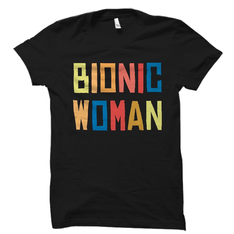 K&ouml;nnte beinhalten: Schwarzes T-Shirt mit dem Text "Bionic Woman" in bunten Blockbuchstaben.