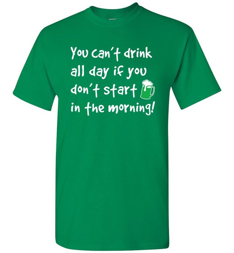 以下が含まれることがあります： 「You can't drink all day if you don't start in the morning!」と書かれた白い文字が入った緑色のTシャツ。テキストの横には緑色のビールジョッキのグラフィックがあります。シャツは無地の緑色です。