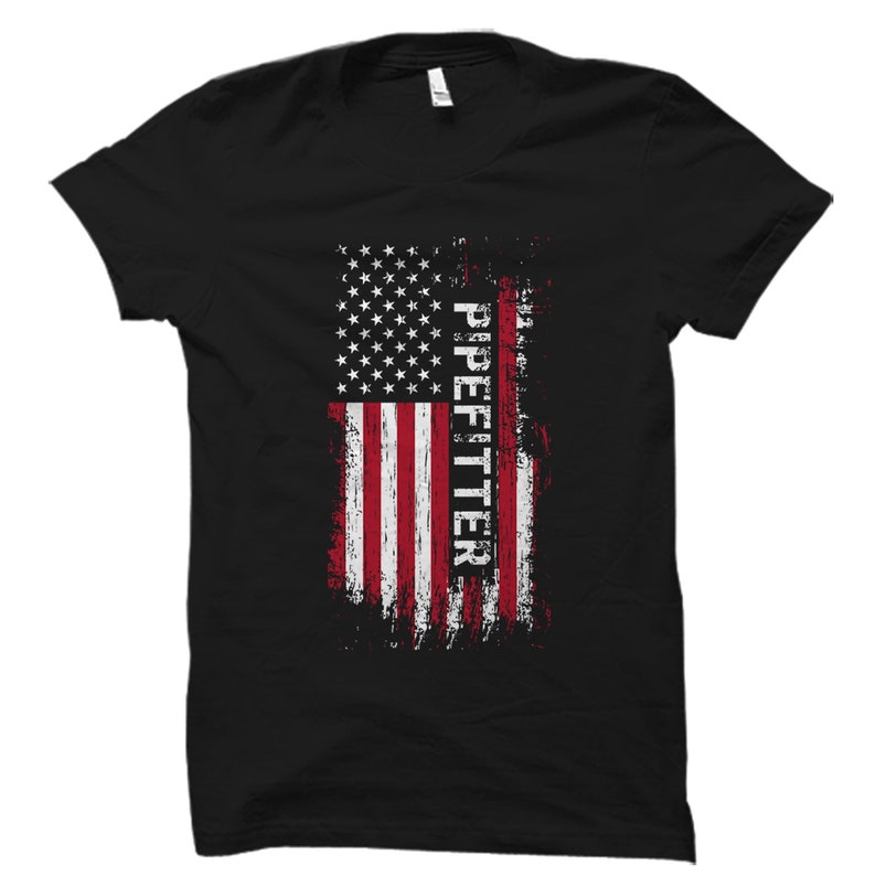 May include: Black t-shirt with a distressed American flag design and the word "Pipefitter" printed vertically down the right side of the flag.