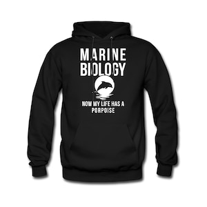 Puede incluir: Sudadera con capucha negra con texto blanco que dice "Marine Biology Now My Life Has A Porpoise" y una silueta blanca de un delfín saltando sobre una ola.