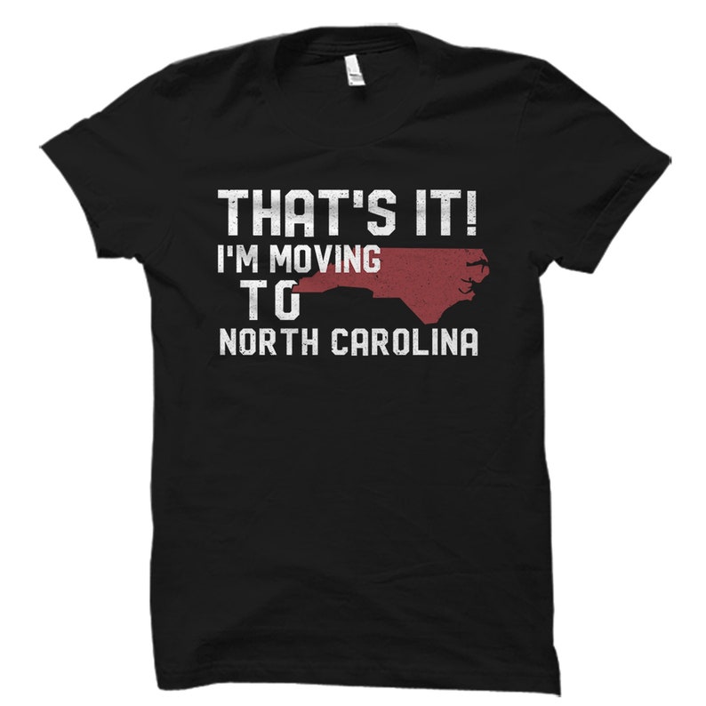 May include: Black t-shirt with the text "THAT'S IT! I'M MOVING TO NORTH CAROLINA" in white, with a red outline of North Carolina. The shirt is a crew neck style.