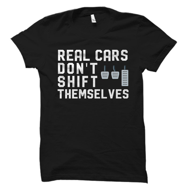 May include: Black t-shirt with white text that reads "Real Cars Don't Shift Themselves". The text is accompanied by a graphic of a stick shift gear.
