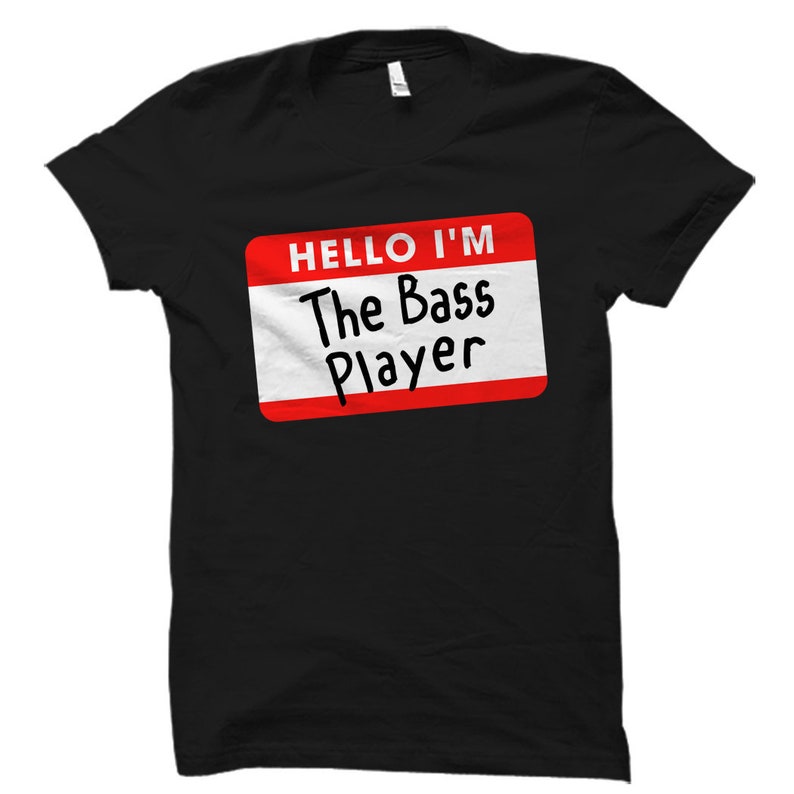 Puede incluir: Camiseta negra con una etiqueta de nombre roja y blanca que dice "Hello I'm The Bass Player".