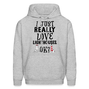May include: A gray hooded sweatshirt with the text "I just really love lighthouses, ok?" printed in black. Two black and white illustrations of lighthouses are below the text.
