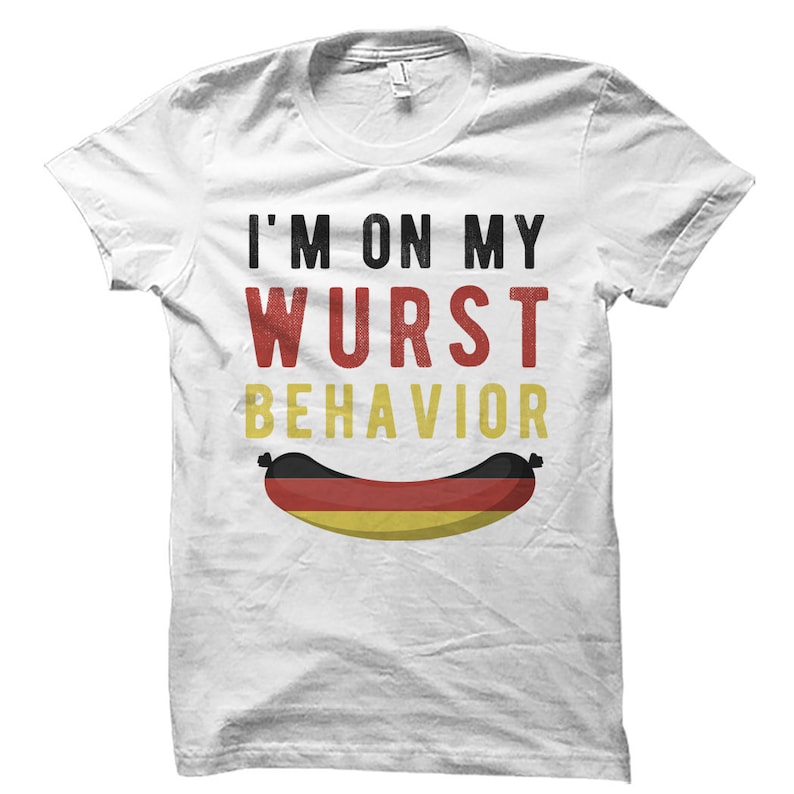 May include: White t-shirt with the text "I'm on my Wurst Behavior" in black and red lettering. A cartoon sausage with the colors of the German flag is below the text.
