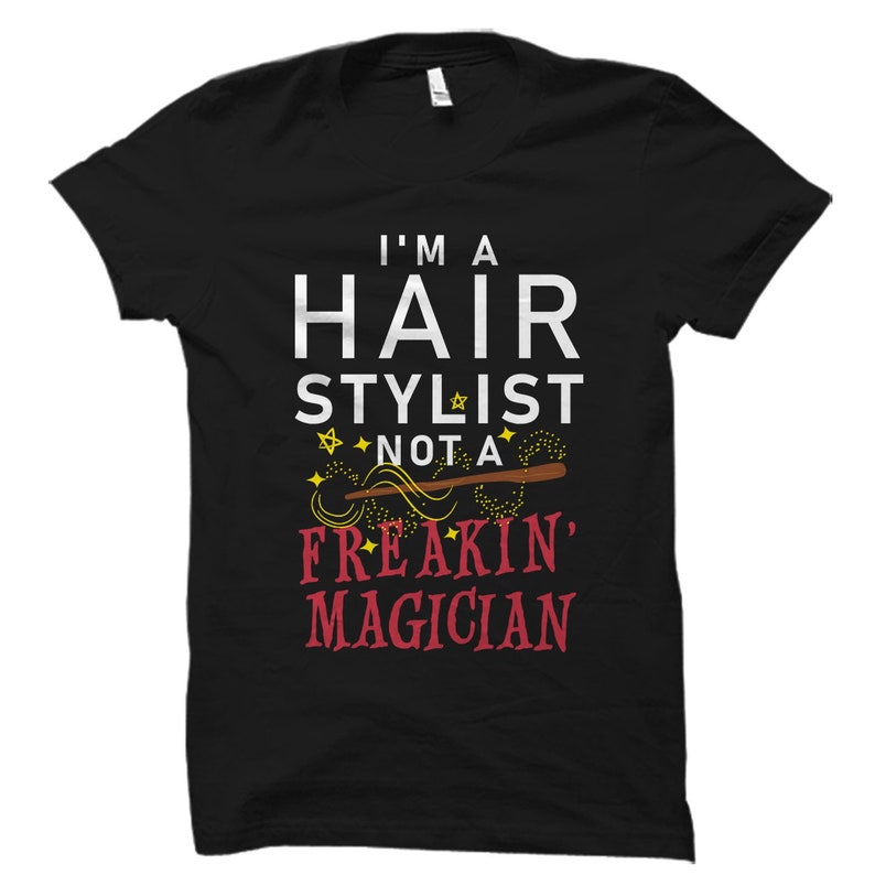 May include: Black t-shirt with white text that reads "I'm a Hair Stylist not a Freakin' Magician". The text is surrounded by yellow stars and a brown and yellow wand.