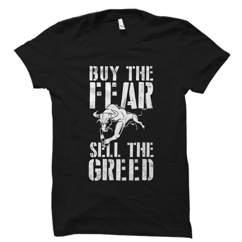 Puede incluir: Camiseta negra con un gr&aacute;fico de toro blanco y el texto "Buy the Fear, Sell the Greed".