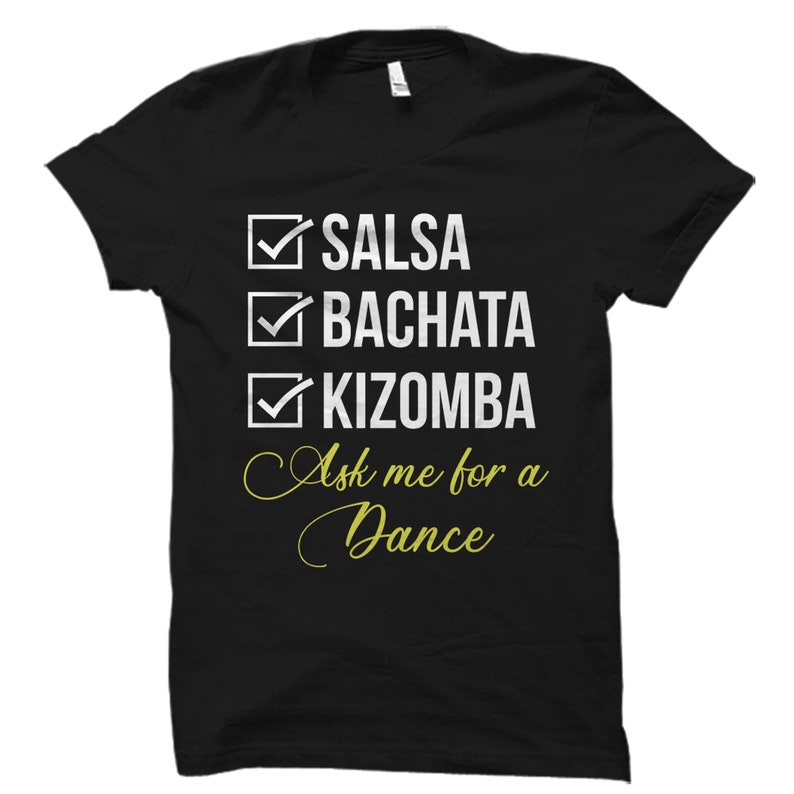 May include: Black t-shirt with a white checklist of dance styles: Salsa, Bachata, Kizomba. The text "Ask me for a Dance" is written in yellow cursive below the checklist.
