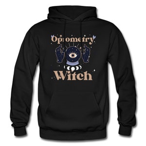 May include: Black hooded sweatshirt with the text "Optometry Witch" in a light brown color. The text is surrounded by a stylized illustration of a hand holding a crystal ball with an eye inside.