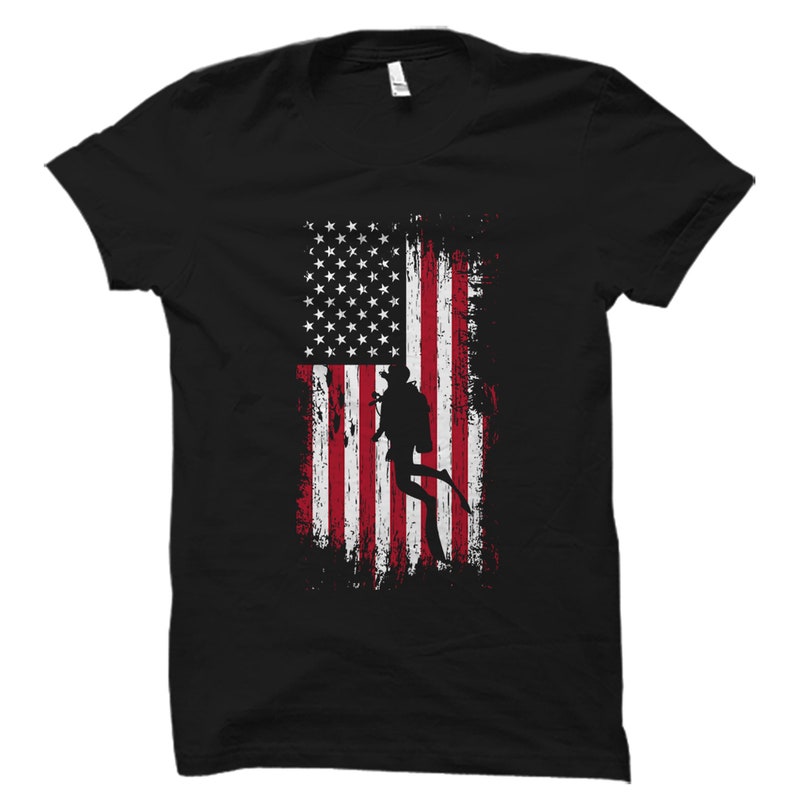 Puede incluir: Camiseta negra con un dise&ntilde;o de bandera estadounidense desgastada y una silueta de un buceador en el centro.