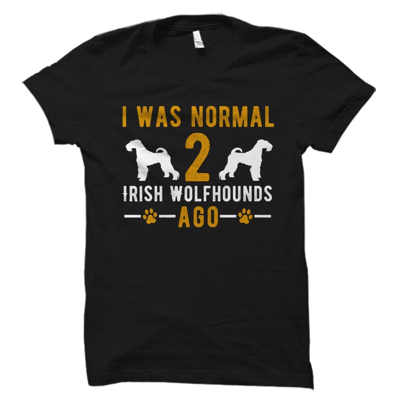 May include: Black t-shirt with the text "I WAS NORMAL 2 IRISH WOLFHOUNDS AGO" in gold and white. The design includes two white Irish Wolfhound silhouettes and paw prints.