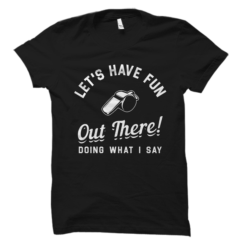 May include: Black t-shirt with white text that reads "Let's Have Fun Out There! Doing What I Say" and a white whistle graphic.