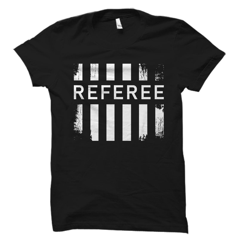 May include: Black t-shirt with a white graphic design of the word "REFEREE" in all caps with five vertical white stripes above and below the word.