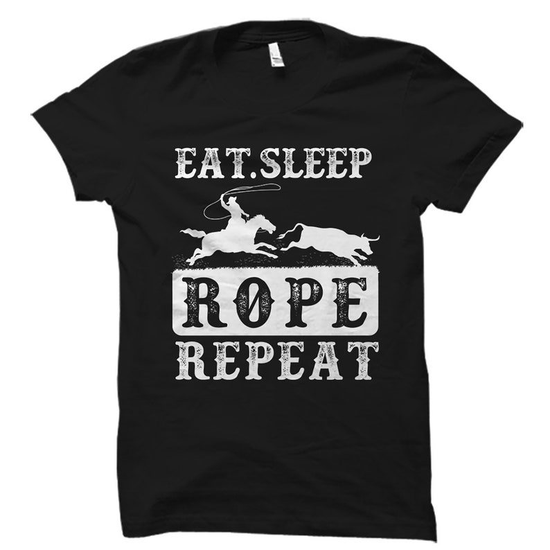 May include: Black t-shirt with a white graphic design that says "Eat. Sleep. Rope. Repeat."  The graphic also includes a silhouette of a cowboy roping a steer.