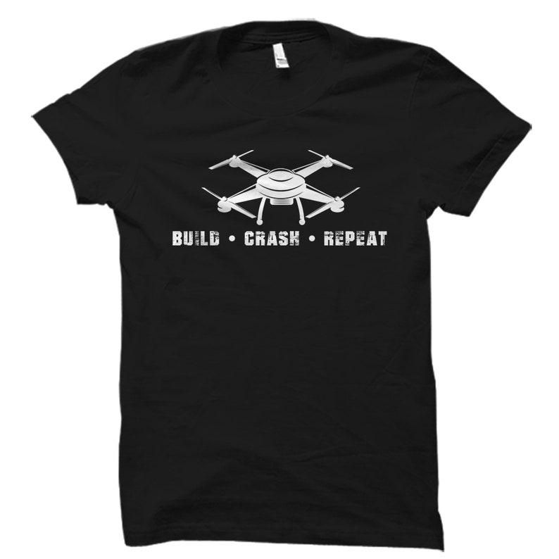 Puede incluir: Camiseta negra con un gr&aacute;fico de dron blanco y el texto "BUILD  CRASH  REPEAT".