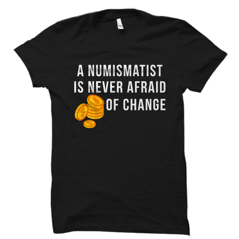 以下が含まれることがあります： 白い文字で「A Numismatist is Never Afraid of Change」と書かれた黒いTシャツ。テキストの隣には、ドルマークの付いた金貨の積み重ねが描かれている。