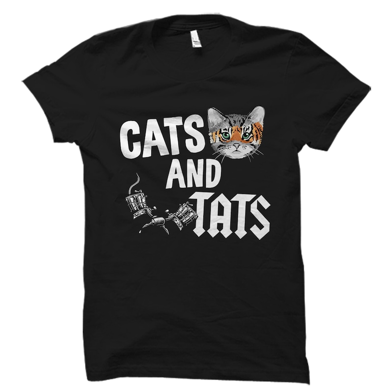 Op de afbeelding: Zwart T-shirt met een wit grafisch ontwerp met een kat met een tatoeagemachine en de tekst "Cats and Tats".