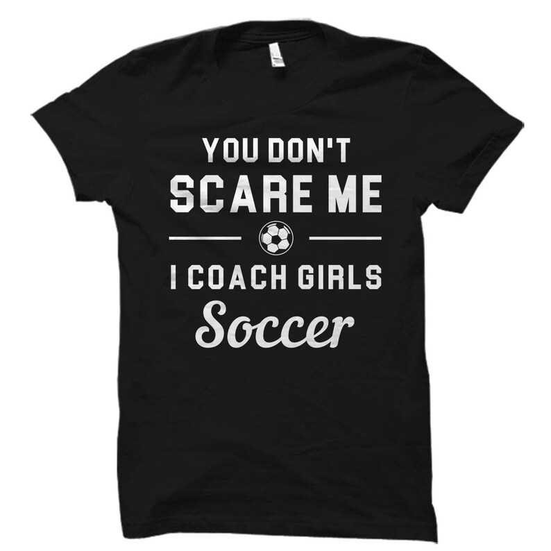 May include: Black t-shirt with white text that reads "You don't scare me I coach girls soccer" and a soccer ball graphic.