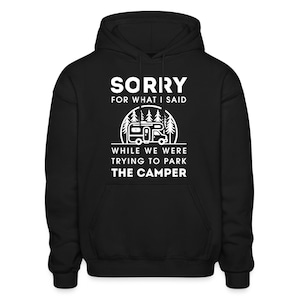May include: Black hooded sweatshirt with white text that reads "Sorry for what I said while we were trying to park the camper". The text is surrounded by a white outline of a camper in a forest.
