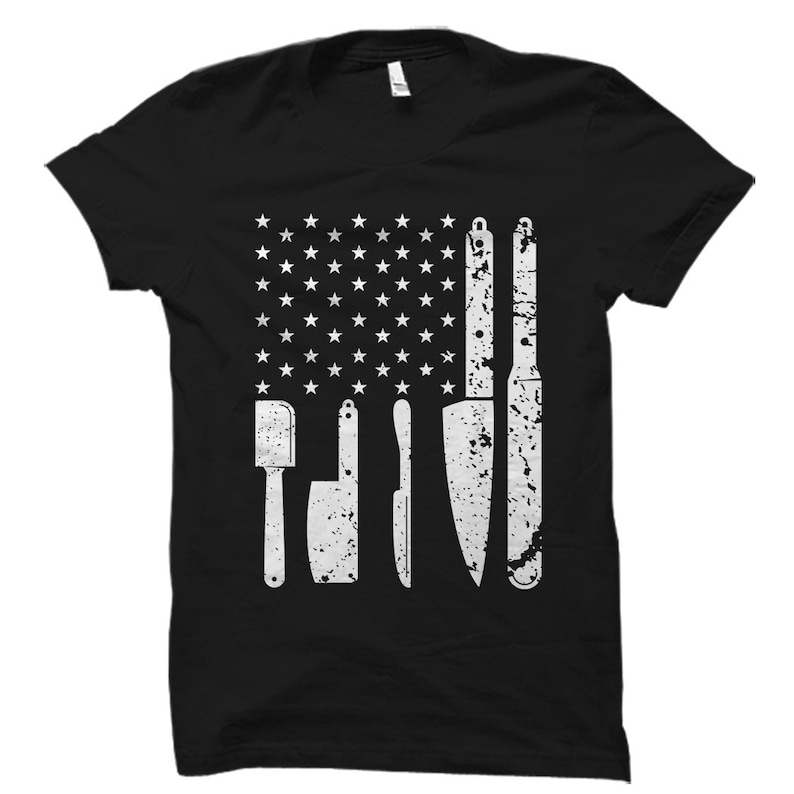 May include: Black t-shirt with a white distressed American flag design featuring a spatula and knives.