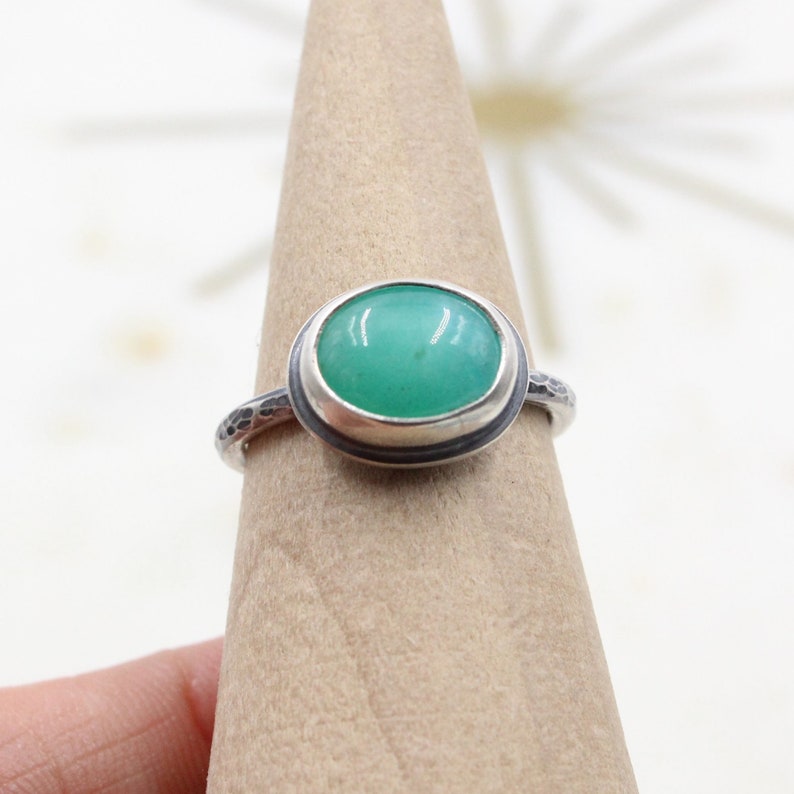 Op de afbeelding: Een zilveren ring met een groene ovale edelsteen gezet in een bezel setting. De ringband heeft een gehamerde textuur.