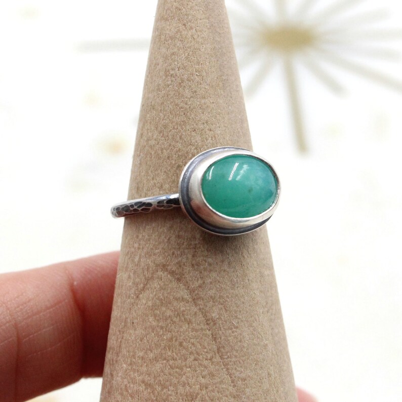 Op de afbeelding: Een zilveren ring met een groene ovale edelsteen in een bezel-setting. De band van de ring is getextureerd.